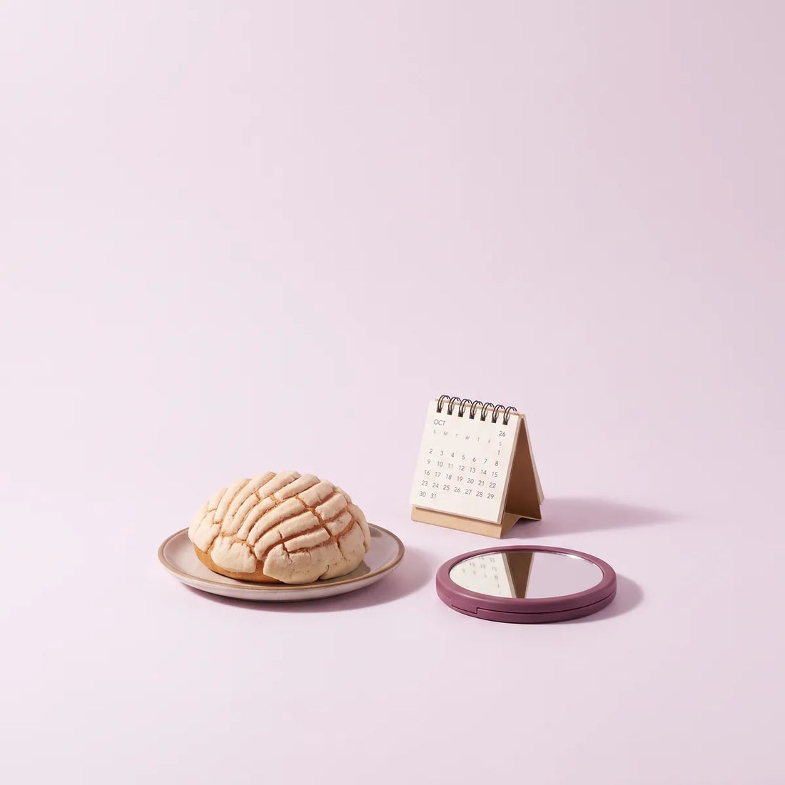 Pan dulce, calendario de escritorio y espejo de mano sobre fondo lila