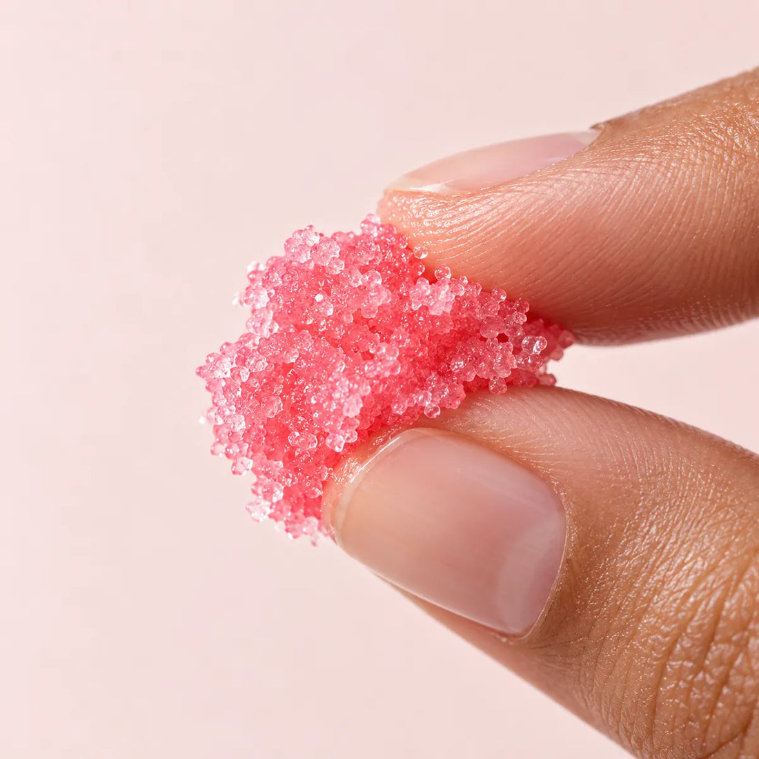Macro de los cristales rosas del exfoliante sobre la yema de los dedos