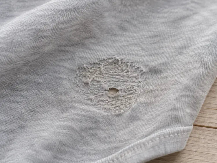 Playera gris con un desgaste circular y un pequeño agujero a la altura del ombligo